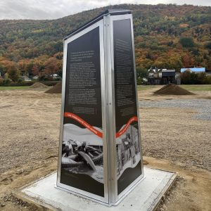 Borne d’interprétation en aluminium avec textes et photographies historiques, devant les montagnes de Petite-Rivière-Saint-François.